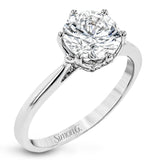 This 18k white gold engagement ring looks deceptively simple at first, but reveals its intricacy upon closer inspection. Accents of .05 ctw of diamonds decorate the sides of the six-prong center stone setting, creating a stunning effect.