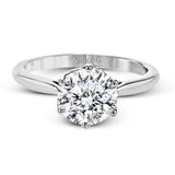 This 18k white gold engagement ring looks deceptively simple at first, but reveals its intricacy upon closer inspection. Accents of .05 ctw of diamonds decorate the sides of the six-prong center stone setting, creating a stunning effect.