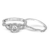 This 18k white gold wedding set has a distinctive design with a milgrain accented bezel center stone setting, .15 ctw pear side stones, and .50 ctw of round brilliant diamonds.