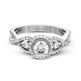 This 18k white gold wedding set has a distinctive design with a milgrain accented bezel center stone setting, .15 ctw pear side stones, and .50 ctw of round brilliant diamonds.