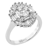 Crafted in 18K white gold, this distinctive ring is an ode to Art Deco design & features a halo of RD diamonds 0.23 ctw, surrounded by a burst of baguette shaped diamonds 0.70 ctw.