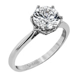 This 18k white gold engagement ring looks deceptively simple at first, but reveals its intricacy upon closer inspection. Accents of .05 ctw of diamonds decorate the sides of the six-prong center stone setting, creating a stunning effect.